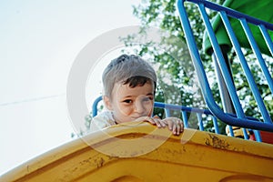 happy child kindergarten boy playing on slide on playground in summer