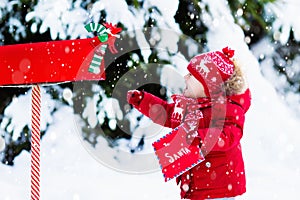 Child with letter to Santa at Christmas mail box in snow