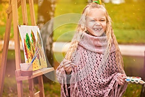 Happy child laughs. joyful little girl artist paints a picture in autumn in the park