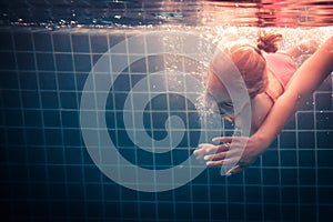 Happy child learning swimming underwater in swimming pool during diving training with helping mother hand