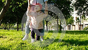 Happy child is learning to walk in the park at sunset. Mother helps the baby to take the first steps