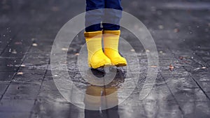 Happy child legs in yellow rubber boots dance and jump in small puddle