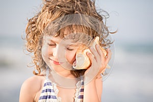 Happy child listen to seashell at the beach photo