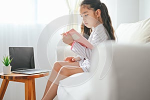 Happy child little asian girl  reading a books on the table in the living room at home. family activity concept