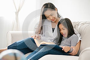 Happy child little asian girl  reading a books on the table in the living room at home. family activity concept