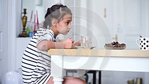 Happy child little girl eat date fruit in the summer home kitchen.