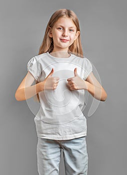 Happy child, little girl showing thumbs up gesture in a white T-shirt