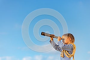 Happy child looking through vintage spyglass against blue sky