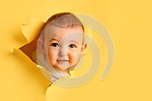 A happy child looks out of a hole in the studio yellow background. Smil