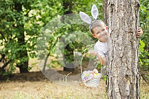 Happy child looks out of a tree holding basket full of colorful easter eggs after egg hunt at spring time. Happy Easter day