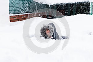 Happy child lying on his back on completely snowy ground. The child is wearing a winter coat with a hood covering his head