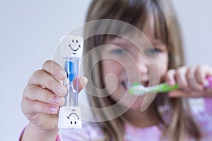 Happy Child measures time while brushes her teeth. Healthy habits, dentalcare concept. Close up photo