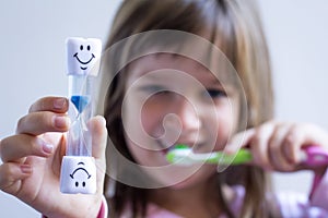Child measures time while brushes her teeth. Healthy habits, dentalcare concept. Close up photo
