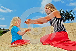 Happy child with mother on heap of rice grains crop.