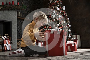 Happy child opens big Christmas gift on Christmas tree background. Joyful boy with Xmas present. New Year time