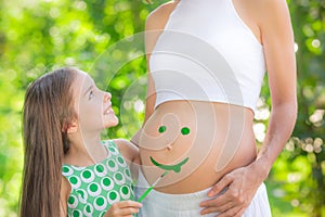 Happy child painting smile on belly of pregnant woman