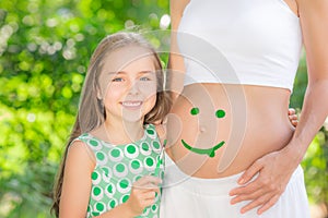 Happy child painting smile on belly of pregnant woman