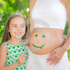 Happy child painting smile on belly of pregnant woman