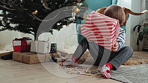 Happy Child in pajamas opens a Christmas present under the Christmas tree