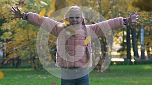 Happy child with pigtails throwing up autumn leaves, joyful childhood time