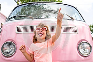 Happy child in pink retro car. Kid hippie. Happy toddler child having fun for travel in pink minivan.