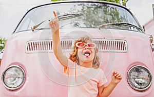 Happy child in pink retro car. Kid hippie. Happy toddler child having fun for travel in pink minivan.