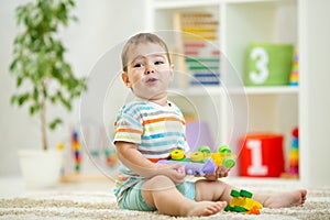 Happy child playing with colorful plastic bricks on the floor. Toddler having fun and building a train out of