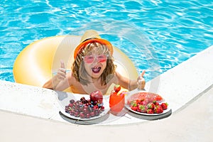 Happy child playing in swimming pool. Summer kids vacation. Summer fruit for children. Little kid boy relaxing in a pool