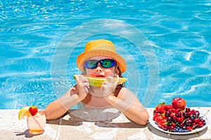 Happy child playing in swimming pool. Summer kids vacation. Summer fruit for children. Little kid boy relaxing in a pool