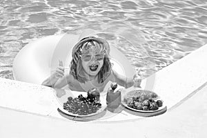 Happy child playing in swimming pool. Summer kids vacation. Summer fruit for children. Little kid boy relaxing in a pool