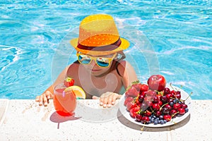 Happy child playing in swimming pool. Summer kids vacation. Summer fruit for children. Little kid boy relaxing in a pool