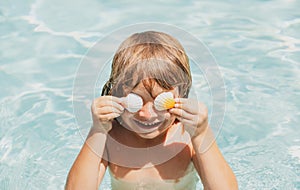 Happy child playing in swimming pool. Summer vacation concept. Covered eyes with shells.