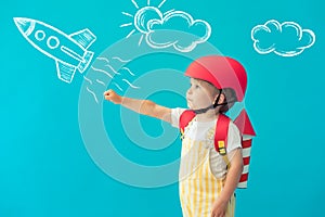 Happy child playing with toy paper wings against blue background