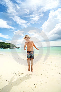 Happy child playing at the tropical sandy beach, jumping and having fun. Summer holiday. Leisure relax time. Tourism