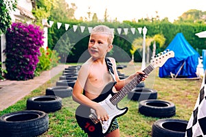 Happy child premiering his summer birthday gift, an electric guitar to play with his friends and enjoy his childhood