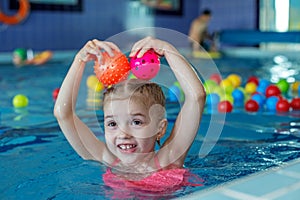 Happy child preschooler learns to swim in swimming pool.Lots of colorful balls