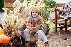 Happy child with pumpkin outdoor in halloween in garden. Smiling girl sit on porch with a pumpkin in her hands. Trick-or-treat. Ha