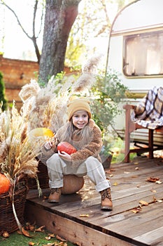 Happy child with pumpkin outdoor in halloween in garden. Smiling girl sit on porch with a pumpkin in her hands. Trick-or-treat. Ha