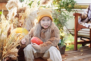 Happy child with pumpkin outdoors in halloween. Smiling girl sit on porch with a pumpkin in her hands. Trick-or-treat. Happy littl
