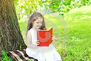 Happy child reading book on grass in summer