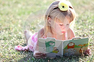 Happy child reading a book on nature in the park