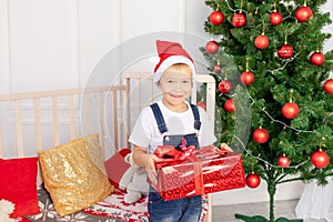 A happy child in a red hat holds a gift for new year or Christmas in the children`s room with a new year`s interior near the