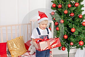 A happy child in a red hat holds a gift for new year or Christmas in the children`s room with a new year`s interior near the