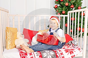 A happy child in a red hat received a gift for new year or Christmas in the children`s room with a new year`s interior near the