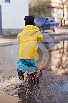 Happy child on a ride rides a scooter through the puddles. Rainy spring. Walks in the open air. no quarantine