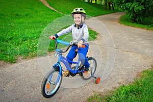 A happy child rides bicycle in green city park outdoors on a footpath