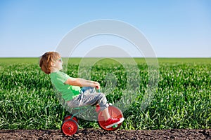 Happy child riding bike outdoor in spring green field