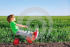 Happy child riding bike outdoor in spring green field