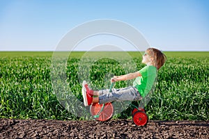 Happy child riding bike outdoor in spring green field