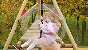 Happy child is riding a swing. Look into the camera and laugh. The girl flies on bungee. Cheerful childhood. Walk in